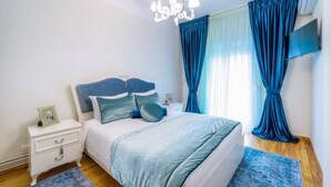 A bedroom with a bed, nightstands, a TV, and a chandelier. - Acropolis Deluxe Apt Must (Thessaloniki)