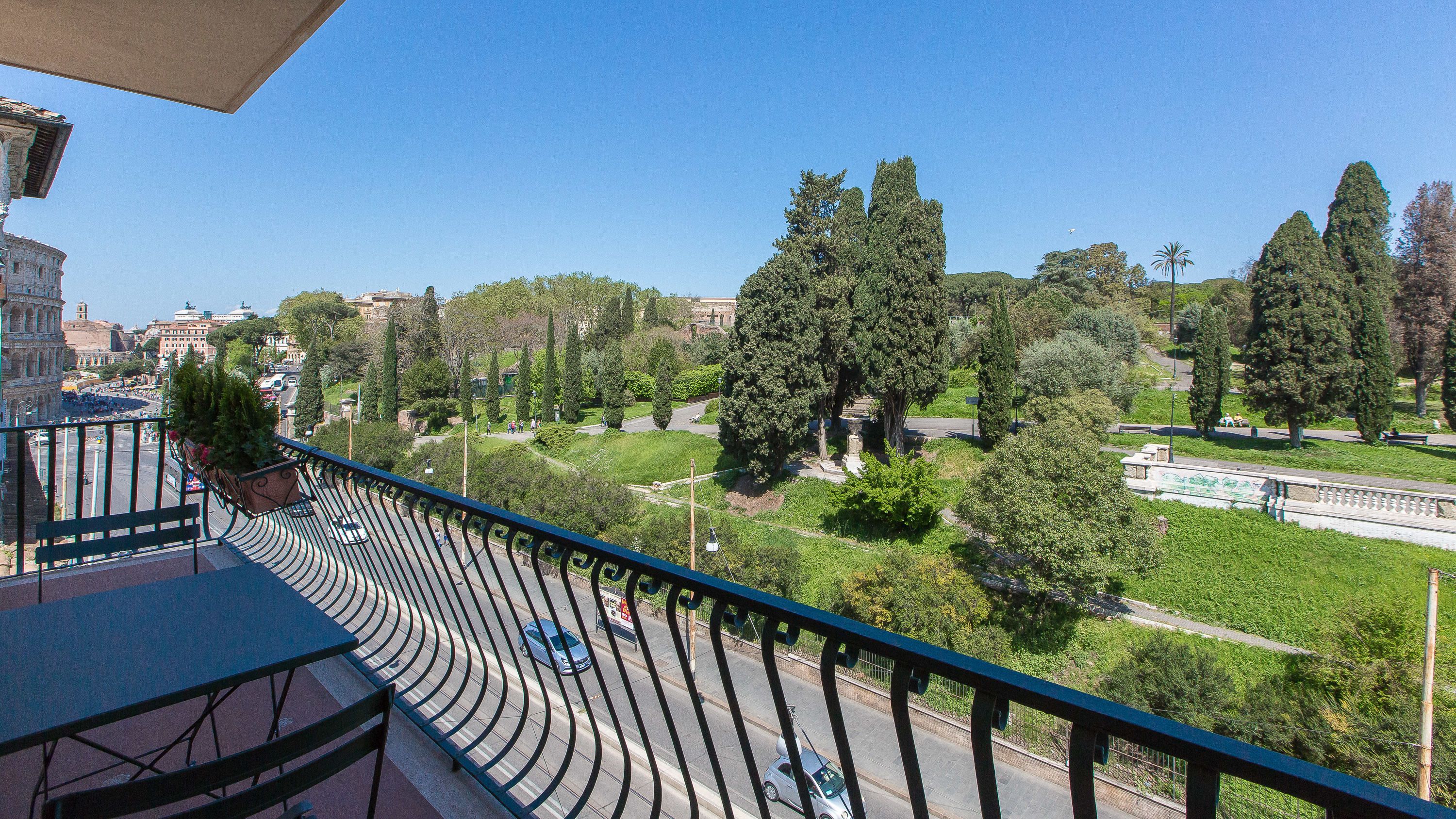 A balcony with a curved railing overlooking a park with trees and a road.