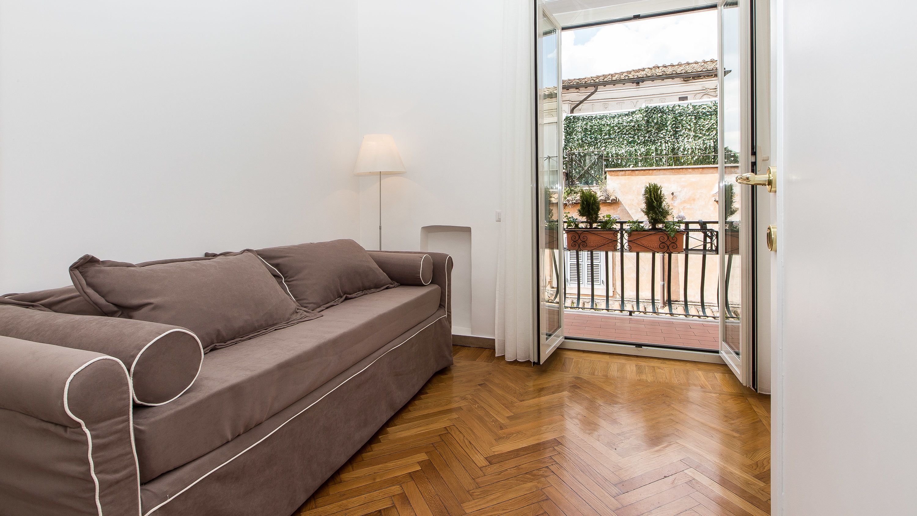A modern living room with a brown sofa, a lamp, and a wooden herringbone floor.