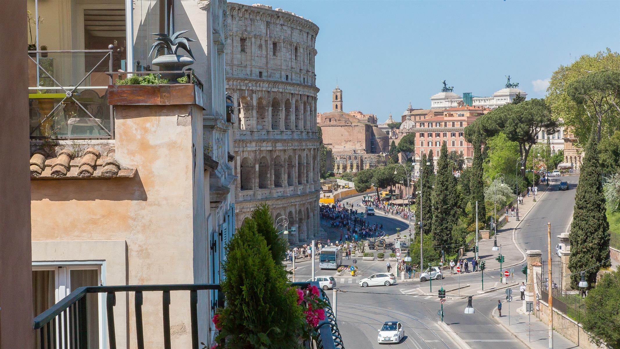 A view of the Colosseum with a busy street in the foreground and a building with balconies.