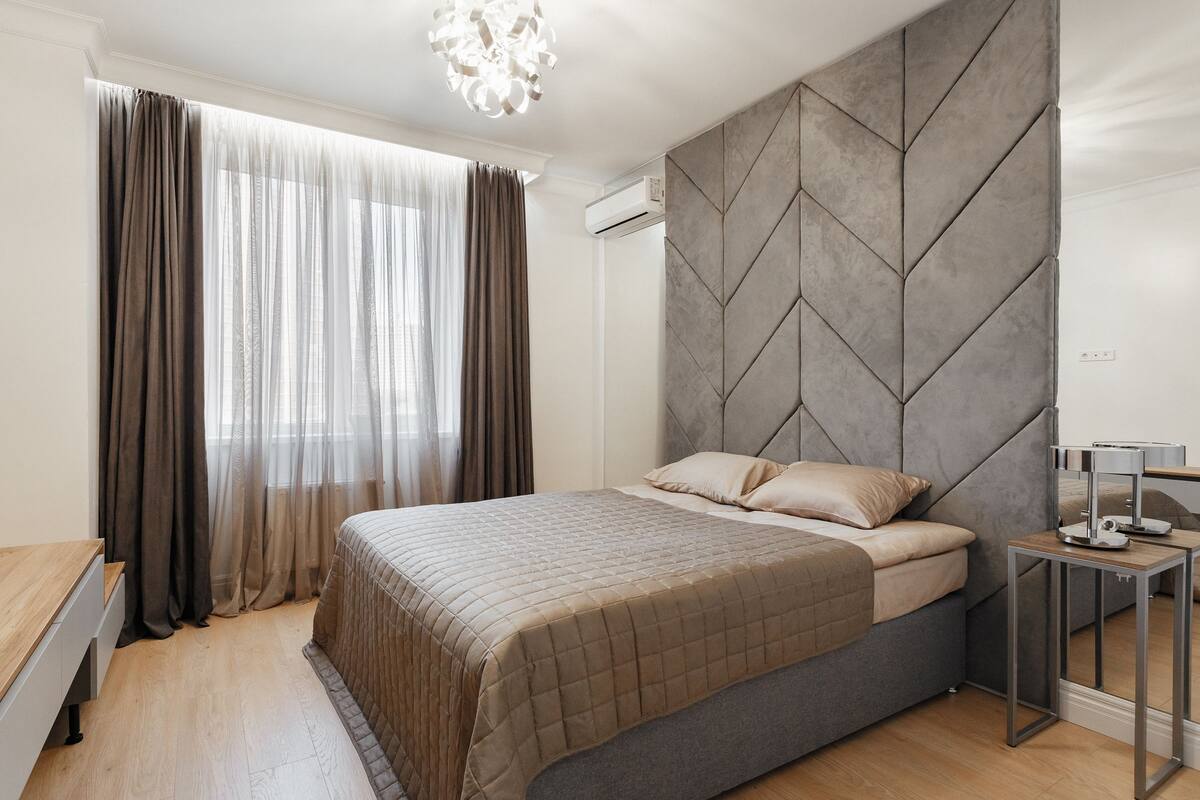 Une chambre moderne avec un lit, une table de chevet, un miroir et une fenêtre avec des rideaux.