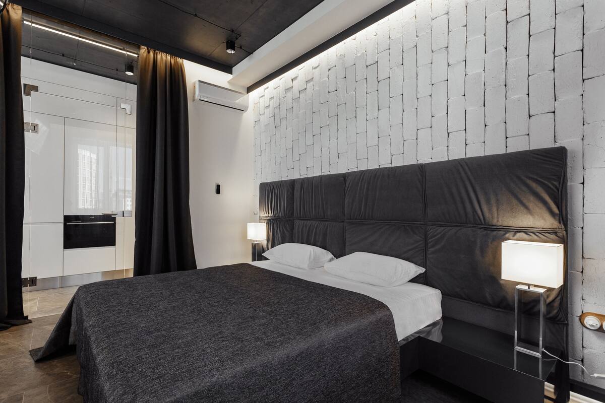 Une chambre d’hôtel moderne avec un grand lit, une table de chevet avec une lampe, une armoire et un mur décoré d’un motif en briques.