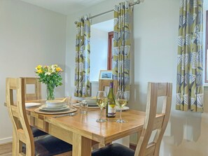 Una mesa de comedor dispuesta con sillas, un florero con flores, copas de vino y una botella de vino.