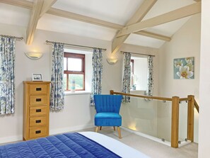 Une chambre à coucher avec un lit, une chaise bleue, une commode en bois et un tableau accroché au mur.