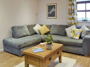 Un canapé d’angle gris agrémenté de coussins décoratifs, une table basse en bois avec un magazine et une plante en pot.