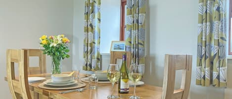 A dining table set with chairs, a vase of flowers, wine glasses, and a bottle of wine.