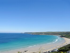 Une plage côtière avec un ciel dégagé, un rivage sablonneux et une vue sur l’océan.