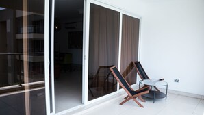Et moderne værelse med en glasdør, der fører til en balkon, et rundt bord og to lænestole.