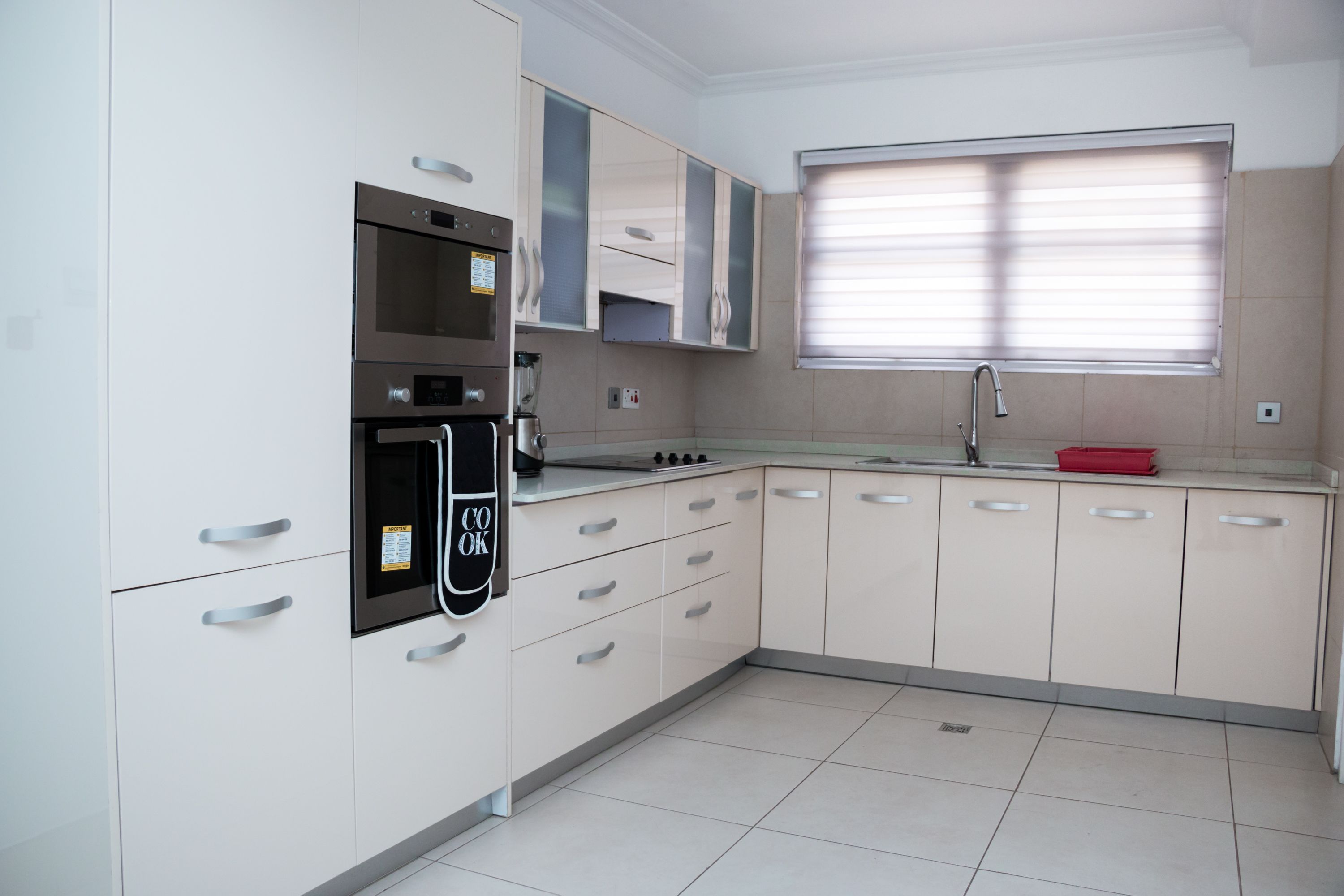 A modern kitchen with white cabinets, stainless steel appliances, and a window with blinds.