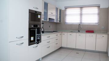 A modern kitchen with white cabinets, stainless steel appliances, and a window with blinds.