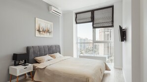A modern bedroom with a large bed, a bedside table with a lamp, a wall-mounted TV, and a cityscape painting. - Arcadia Dream Apartments (Odesa)