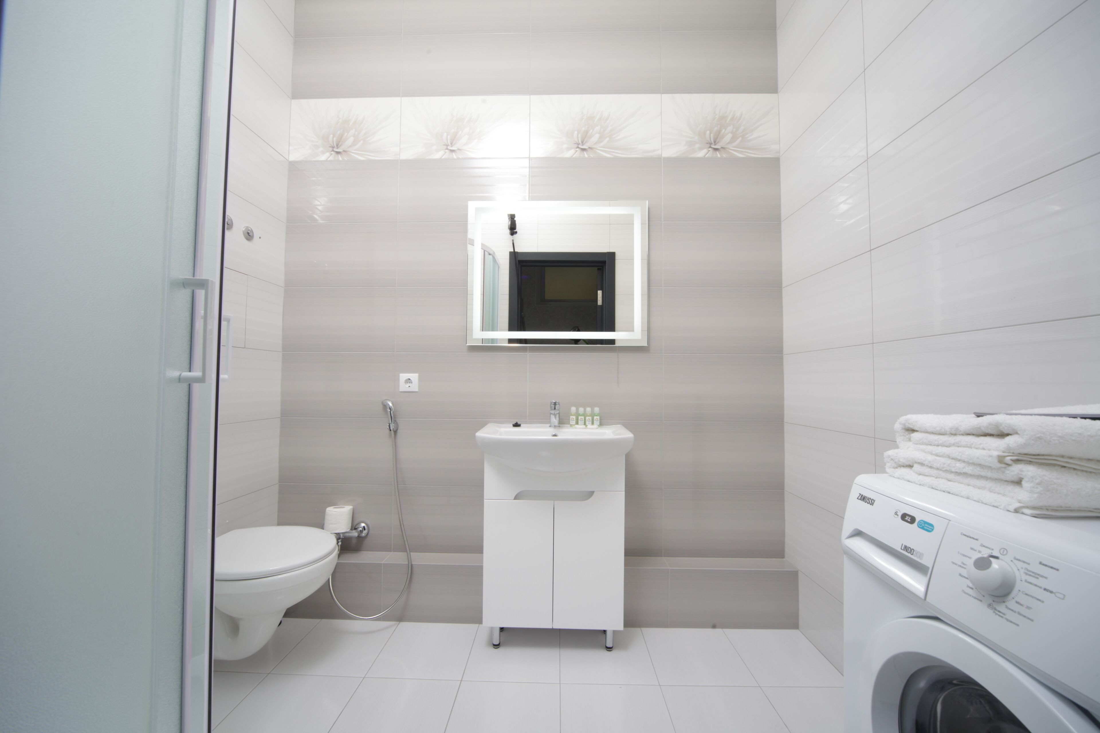 Une salle de bain moderne équipée de toilettes, d’un lavabo, d’un miroir et d’un lave-linge.