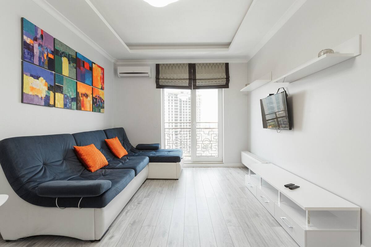 Uma sala de estar moderna com um sofá azul escuro, almofadas laranja, uma mesa de console branca e uma pintura abstrata colorida na parede.
