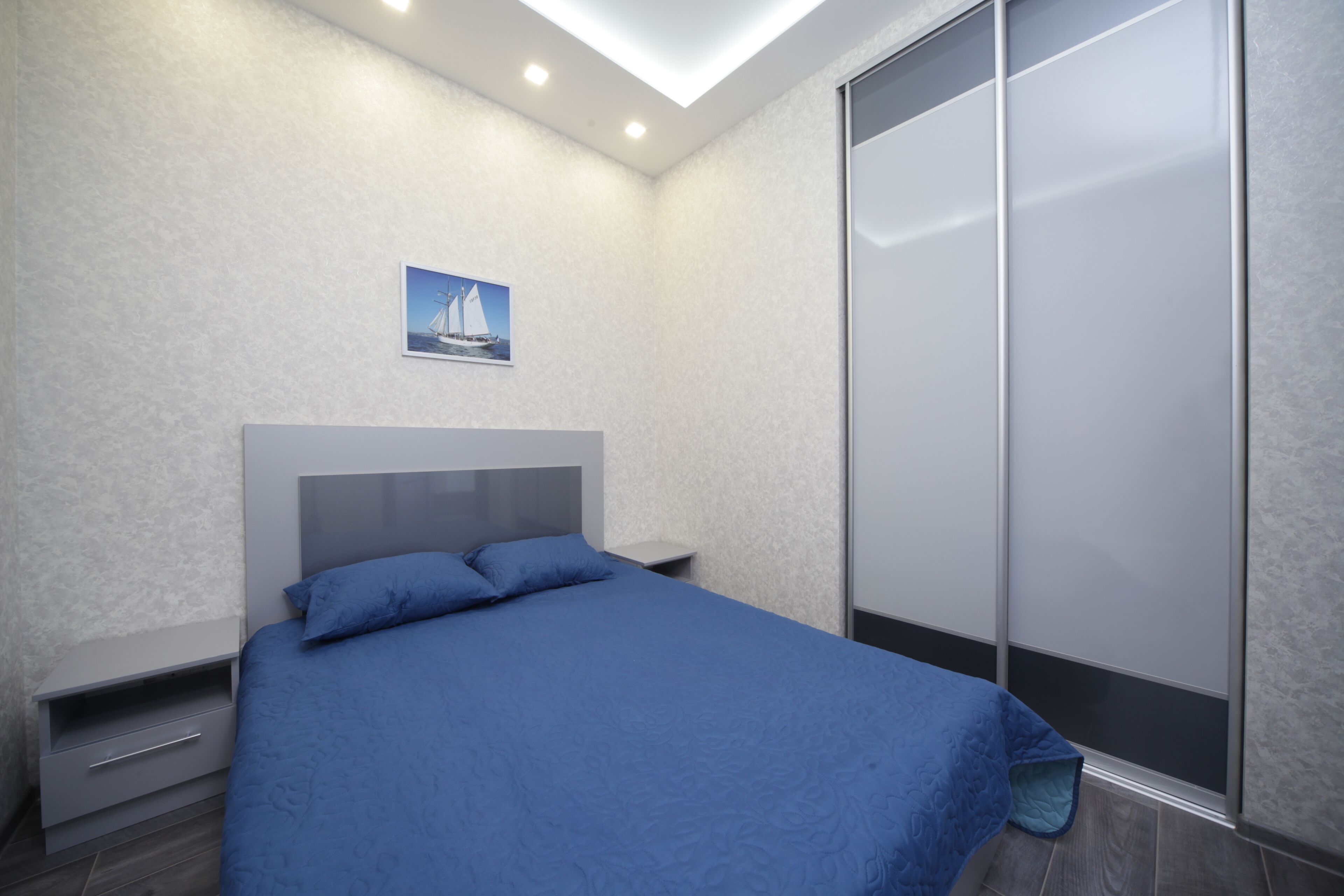 A bedroom with a bed, a nightstand, a drawer unit, and a sliding door closet.