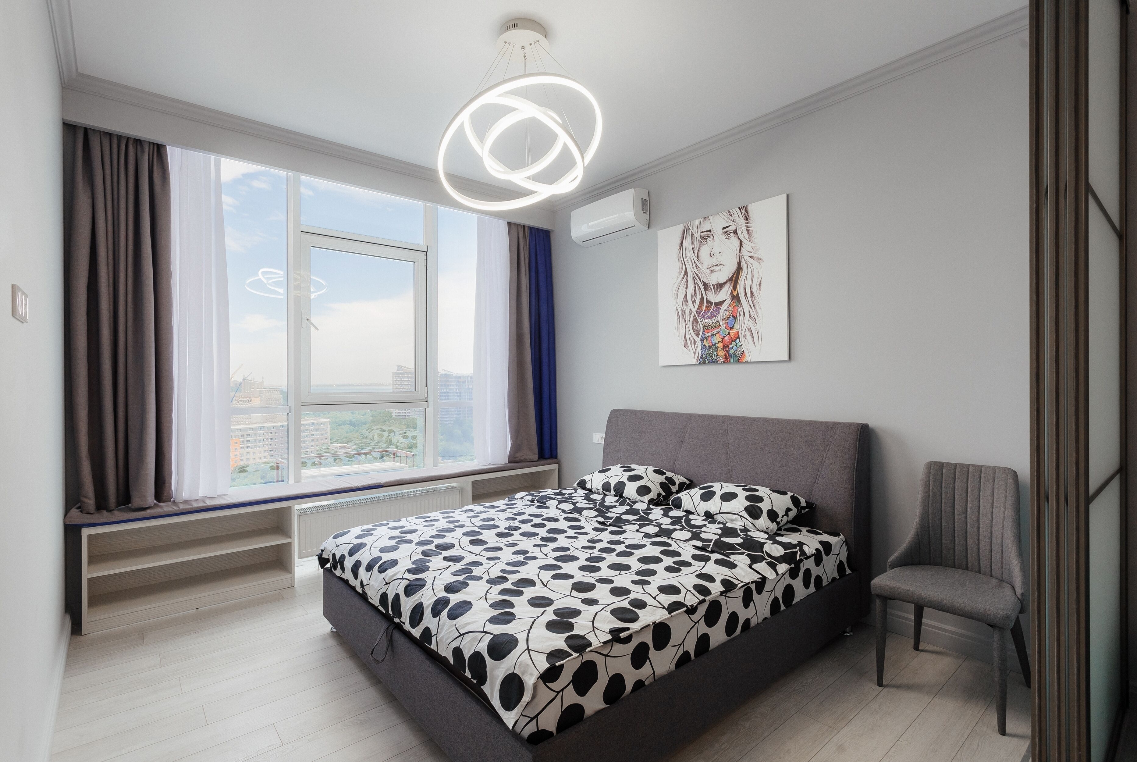 Un dormitorio moderno con una cama grande, una silla, una ventana con cortinas e iluminación en el techo.