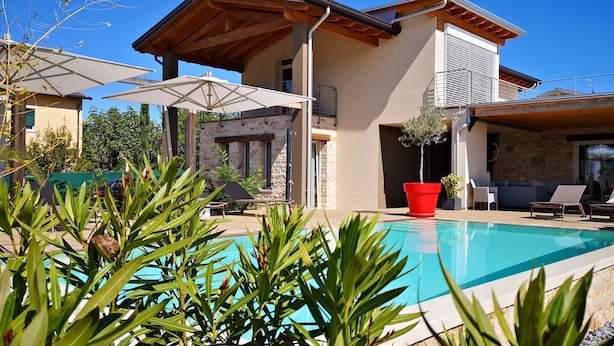 Uma área de piscina moderna com espreguiçadeiras e guarda-sóis, rodeada por vegetação.