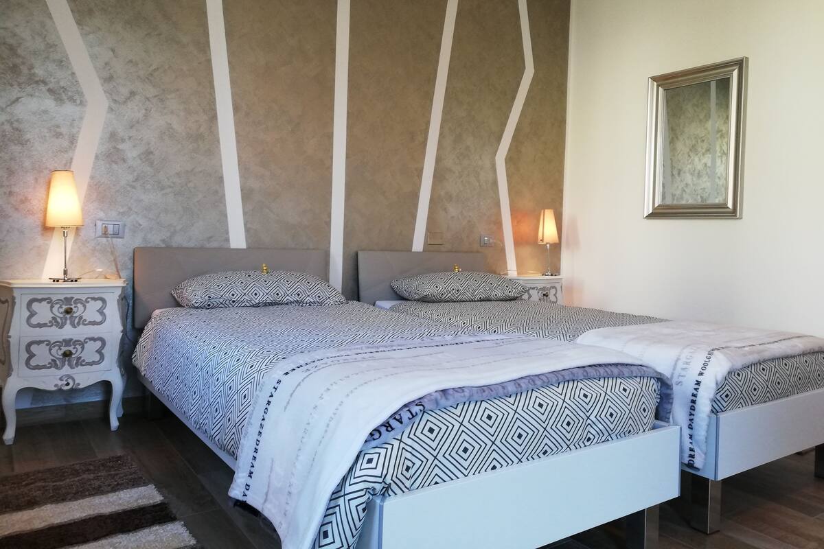 A double bed with patterned bedding, two bedside tables with lamps, a framed picture on the wall, and a textured wall design.