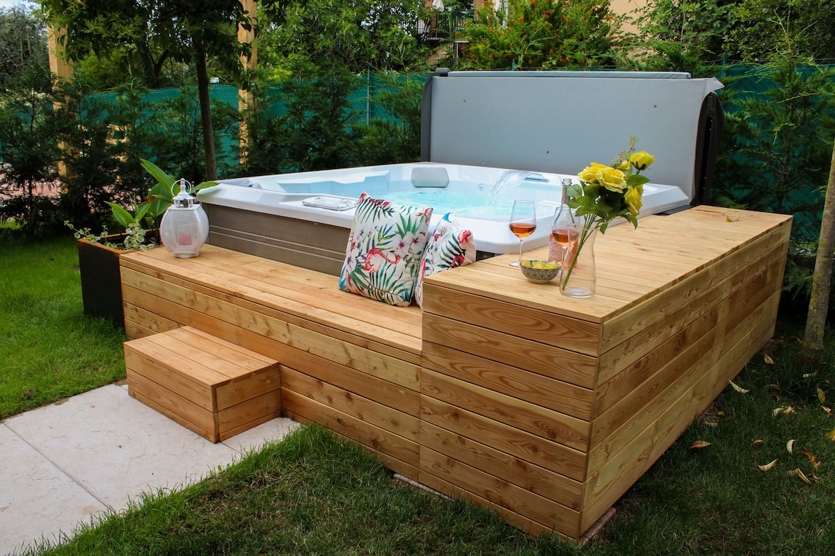 A hot tub with a wooden deck, a glass of wine, and a vase with flowers.