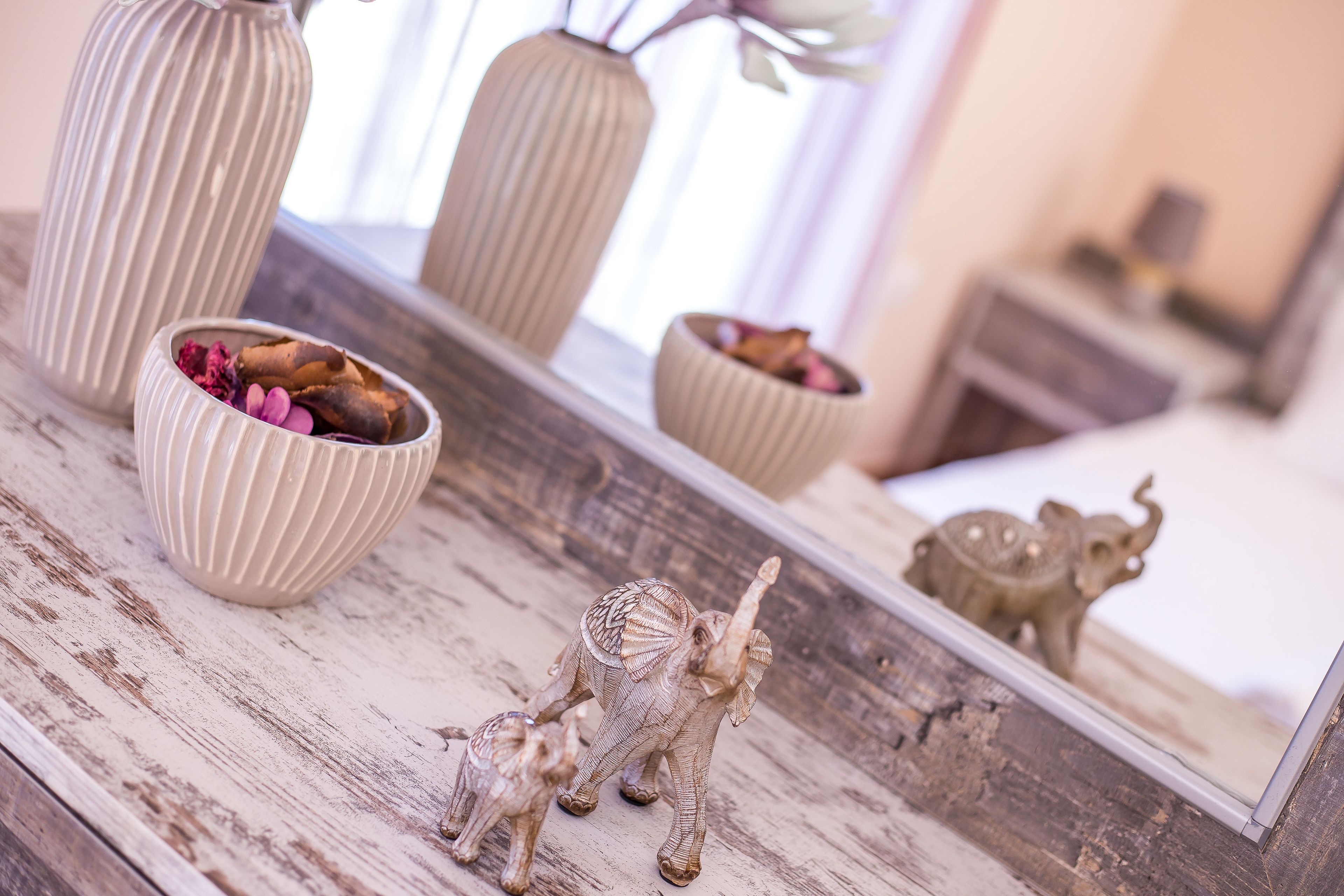 Una mesa de madera con objetos decorativos, incluyendo un florero, un cuenco con flores secas y una pequeña figurita de elefante.