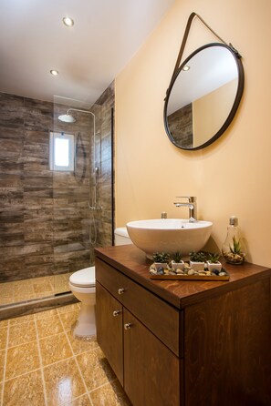 Une salle de bain avec un meuble-lavabo en bois, un miroir rond, un lavabo et une douche.