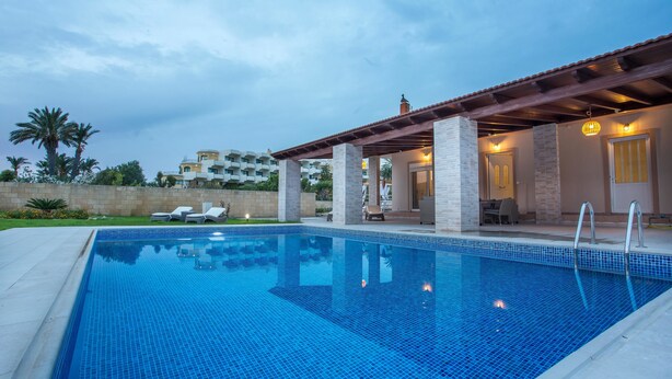 Uma piscina com deck revestido, espreguiçadeiras e área de varanda coberta.