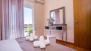 Quarto de hotel com cama, mesa de cabeceira com espelho, porta de madeira e janela com cortinas.