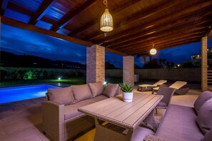 Une terrasse extérieure avec une piscine, des meubles en osier et des guirlandes lumineuses.