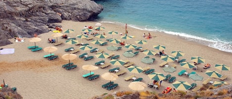 Una playa con numerosos sombrillas y sillas de playa, terreno rocoso y vistas al mar.