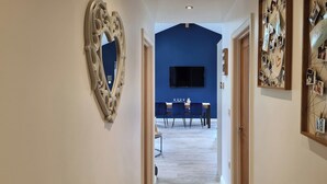 Un pasillo con una pared azul decorativa, un espejo grande y una zona de comedor con televisión.