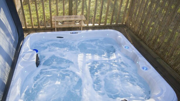 Un jacuzzi con un banco de madera y una valla de bambú al fondo.