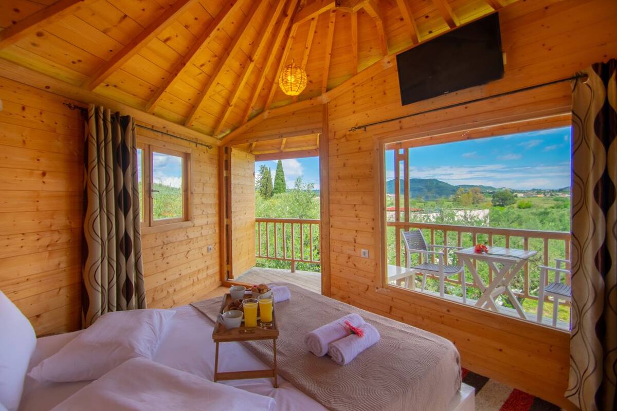 Une chambre dans un chalet en bois, avec un lit, un plateau de petit-déjeuner et un balcon offrant une vue sur la verdure.