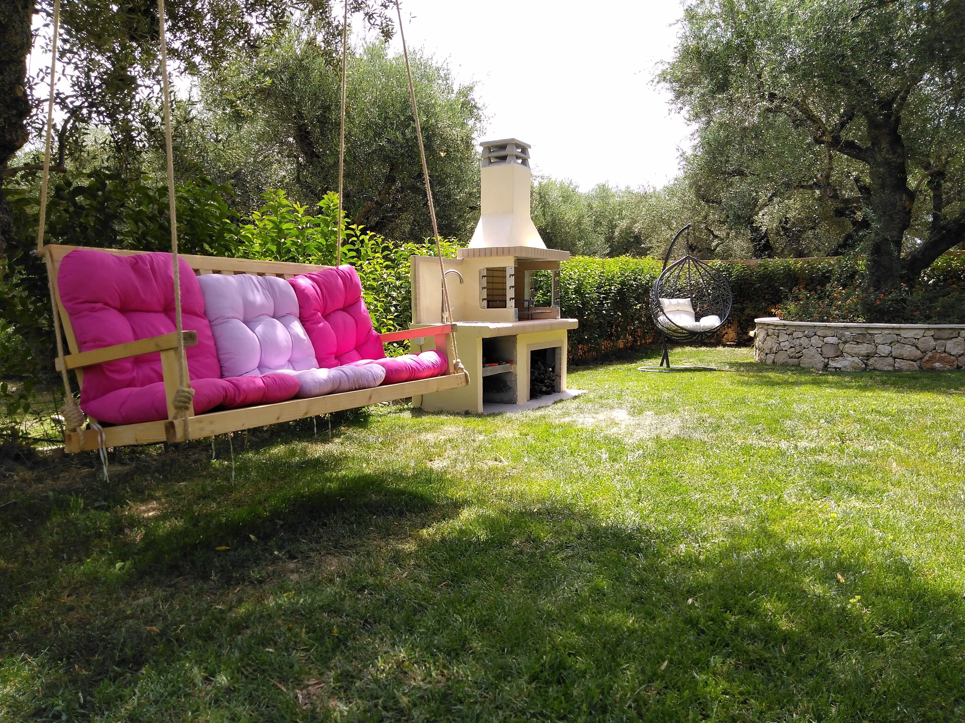 Un jardín con un columpio, un muro de piedra y una pequeña construcción con chimenea.