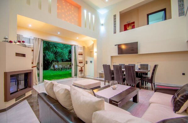A spacious living area with a fireplace, a dining table with chairs, and a view of a green garden.
