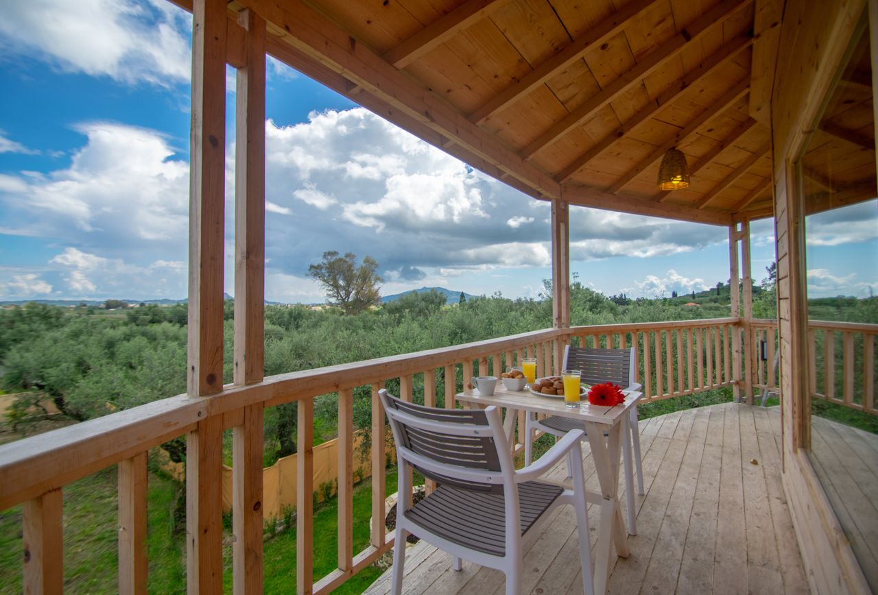 A wooden deck with a table and chairs, overlooking a lush landscape with trees and hills.