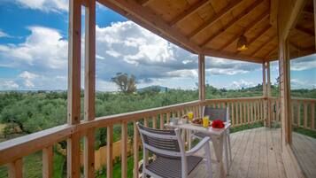 A wooden deck with a table and chairs, overlooking a lush landscape with trees and hills.