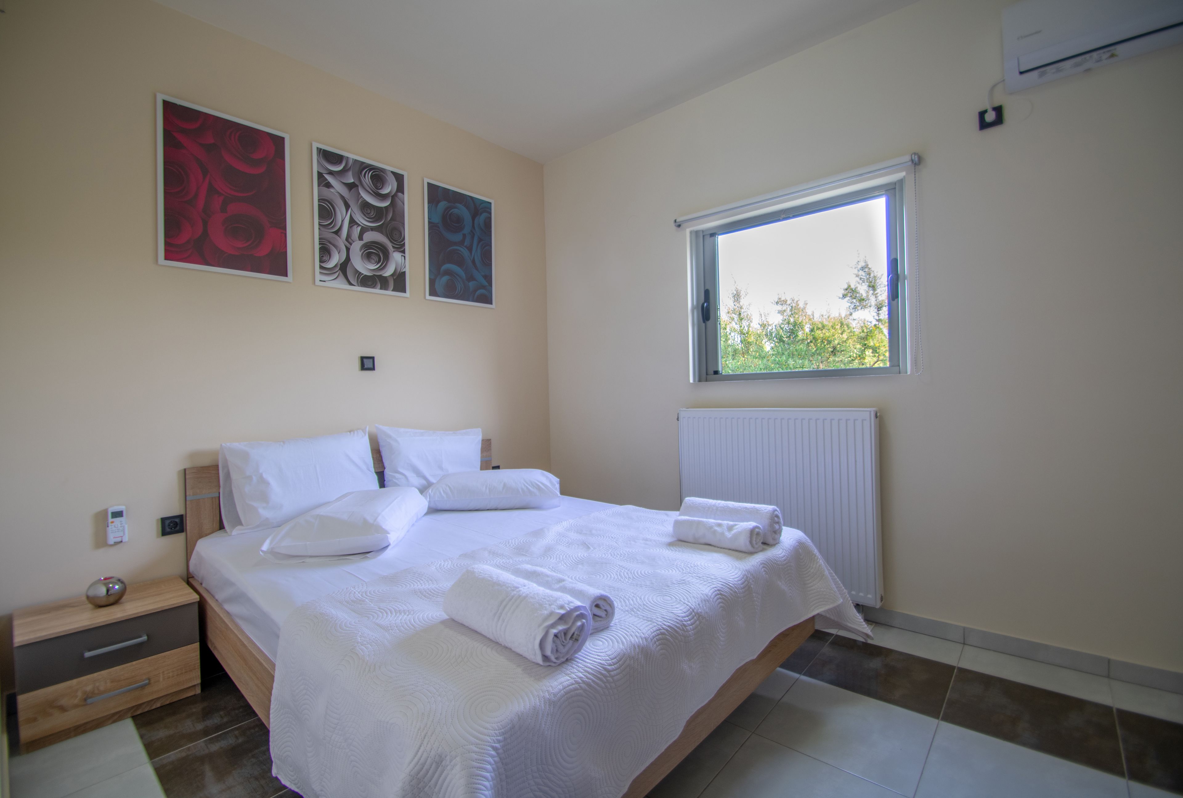 Een slaapkamer met een groot bed, een nachtkastje, een raam met uitzicht en drie kunstwerken aan de muur.