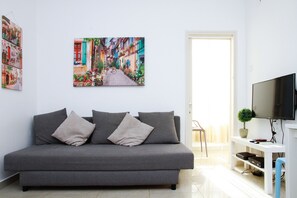 A modern living room with a grey sofa, a flat-screen TV, and a painting of a colorful street scene.