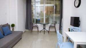 Ein modernes Wohnzimmer mit einer Couch, einem kleinen Tisch, zwei Stühlen, einem Fernseher und einem großen Fenster mit Vorhängen.