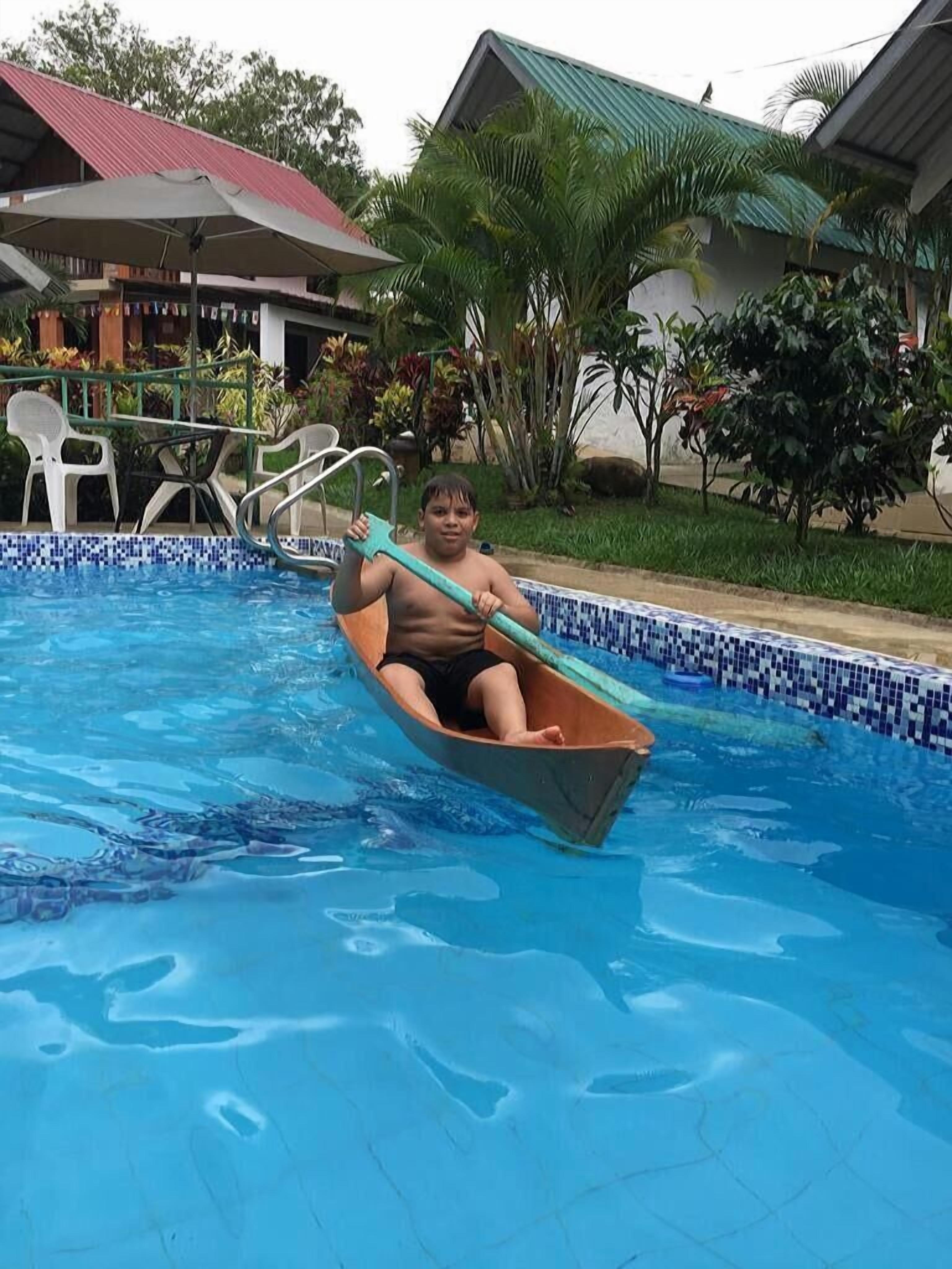 Eine Person in einem Boot in einem Schwimmbecken mit einer gefliesten Kante und einem Gebäude im Hintergrund mit einem grünen Dach.