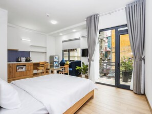 A modern hotel room with a bed, a small kitchenette, a dining area, and a balcony with curtains. - Amazing NYT Home Balcony Cozy Studio (Hanoi)