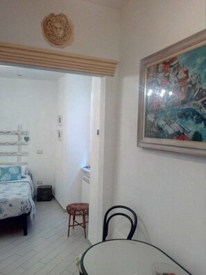 A bedroom with a bed, a small table, and a chair. There is a painting on the wall and a decorative item above the bed. - La Stiva Affittacamere (Riomaggiore)