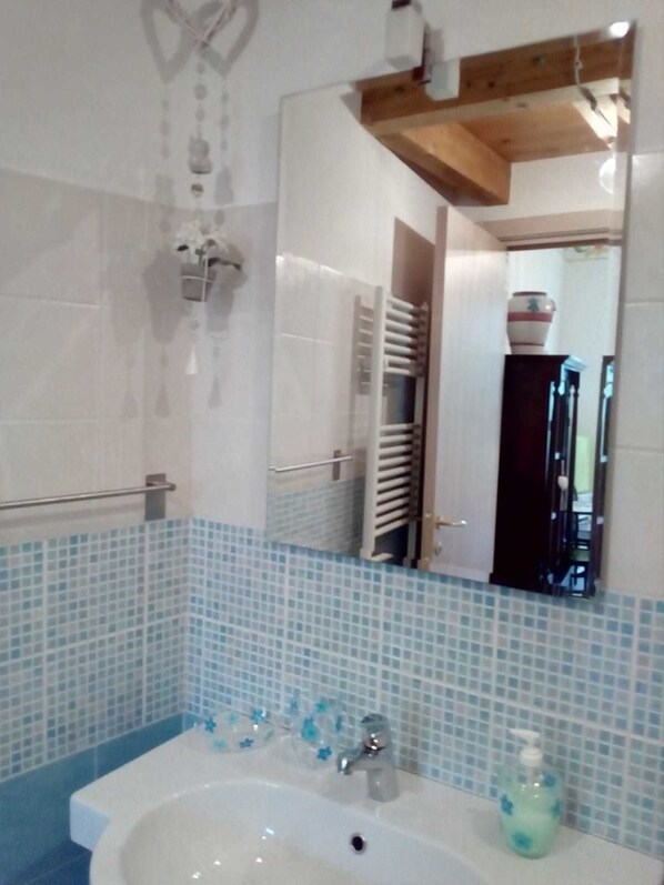 A bathroom with a white sink, blue-tiled walls, a wooden ceiling, and a mirror reflecting a towel rack and a door.