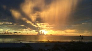 A sunset over a beach with silhouettes of people and vegetation. - Sunsets on the Sand (Indian Shores)