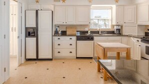 A modern kitchen with white cabinetry, a built-in dishwasher, a double-door refrigerator, and a wooden table. - Sunsets on the Sand (Indian Shores)