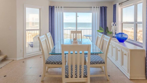 A dining area with a glass table and chairs, a view of the beach, and a balcony with curtains. - Sunsets on the Sand (Indian Shores)