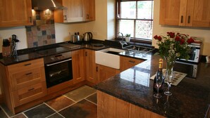 A kitchen with wooden cabinets, a stainless steel range hood, a sink, and a window with blinds.