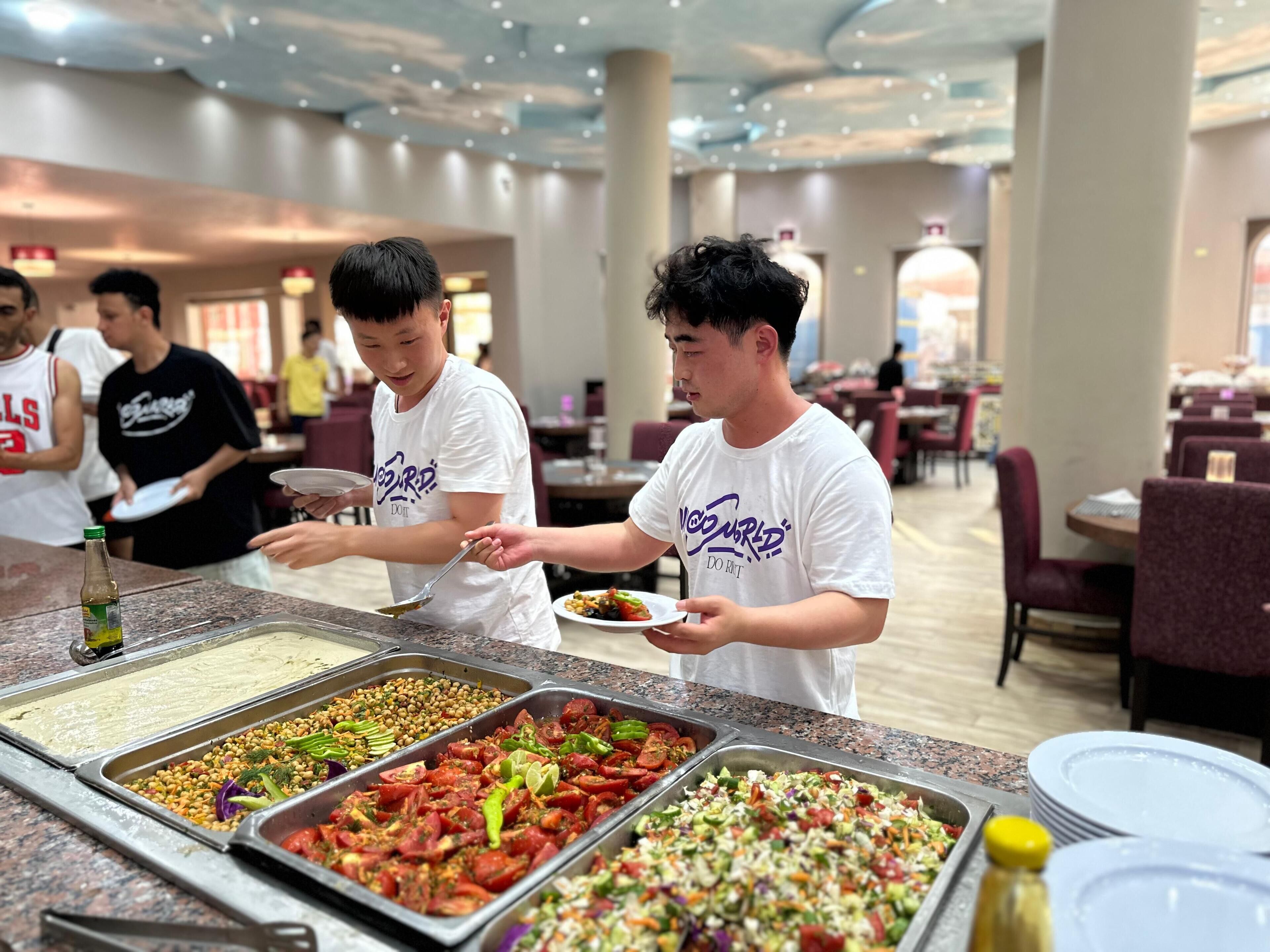 A buffet area with various food options and people serving themselves.
