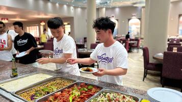 A buffet area with various food options and people serving themselves.