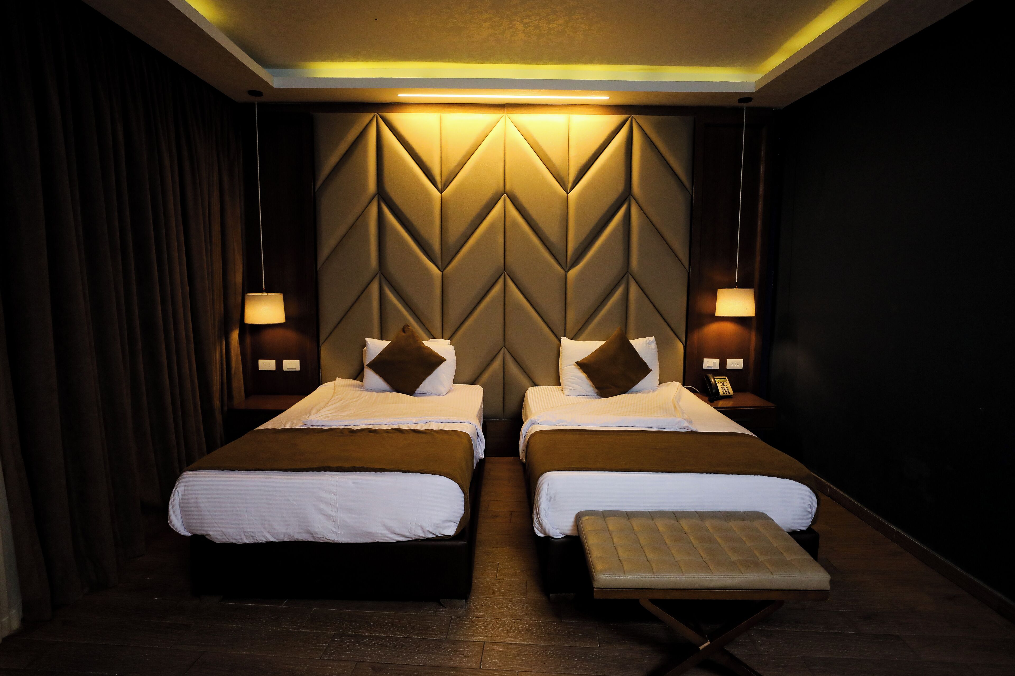 Een hotelkamer met twee bedden, een bankje en een muur met een geometrisch patroon.