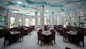 Un restaurant spacieux avec des tables rondes, des chaises rouges et un plafond décoré de motifs nuageux.